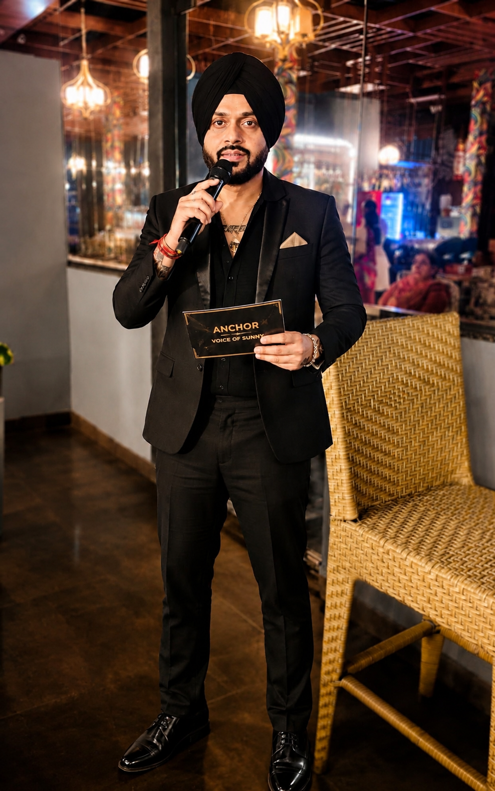 Sunny — Dapper Sikh Emcee in black suit and turban holding a microphone at an event